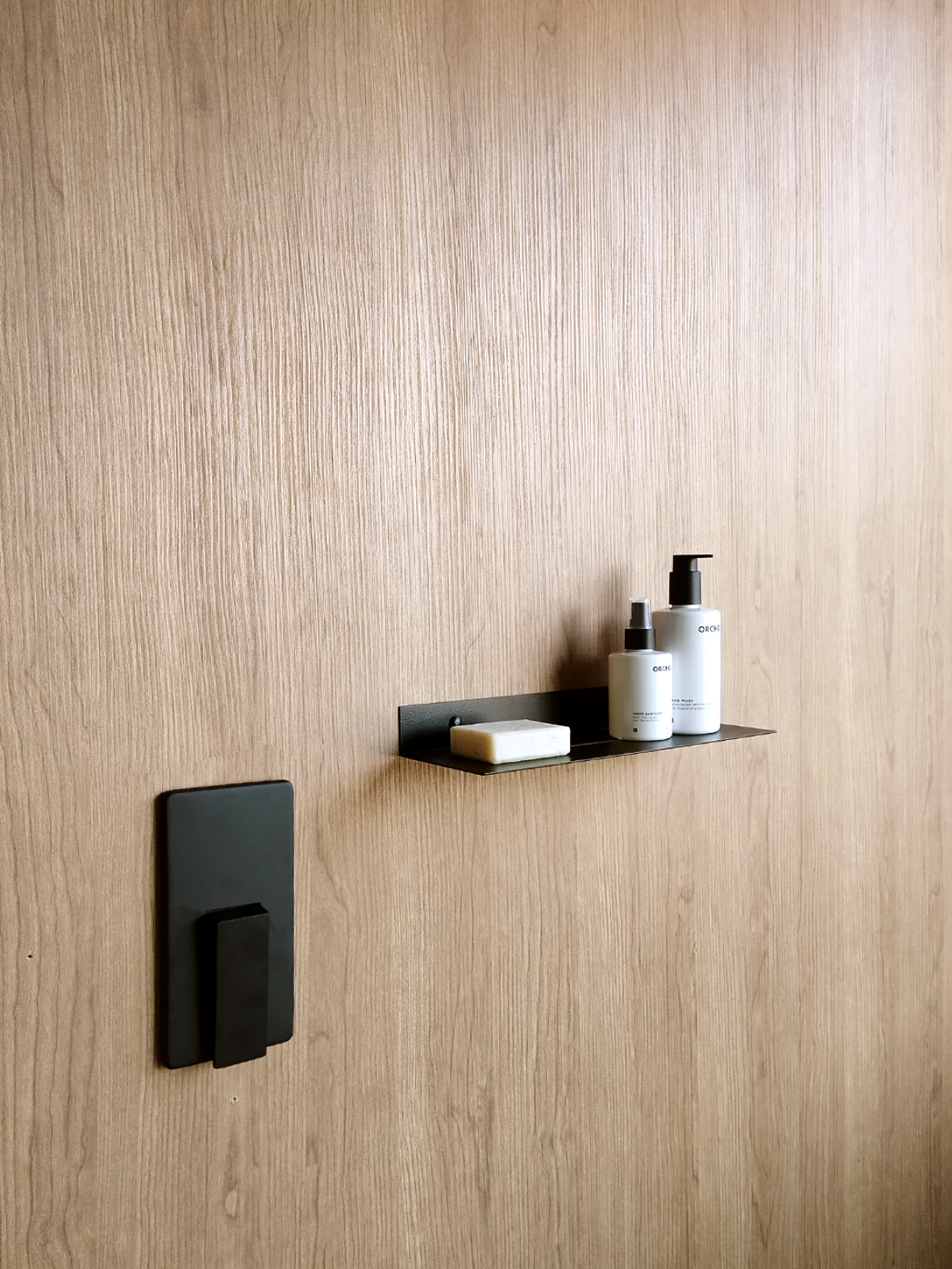 Black steel bathroom shelf or black steel shower shelf or black steel shower caddy next to black shower mixer. The black shower shelf holds artisanal soap and two soap dispensers from mr Price home bathroom in a bathroom design store in Johannesburg