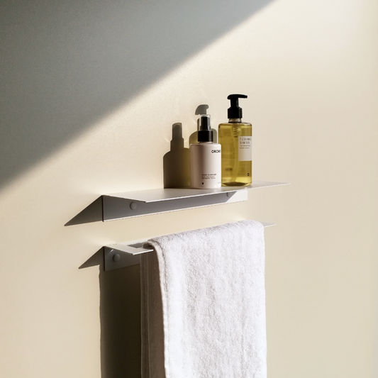 a white steel bathroom shelf in a modern bathroom design in johannesburg. The bathroom shelf has a white soap dispenser from Mr Price Home and a yellow soap dispenser from Mr Price Home. The black metal towel shelf has a black metal towel holder holding a white towel.