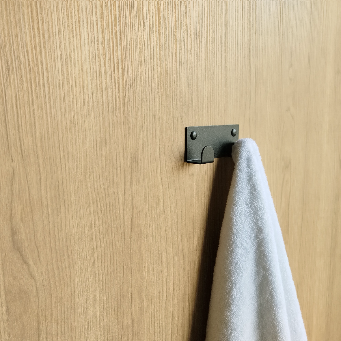 A towel hook in South Africa or a black wall hook is hanging a white bath towel in a furniture design store in South Africa