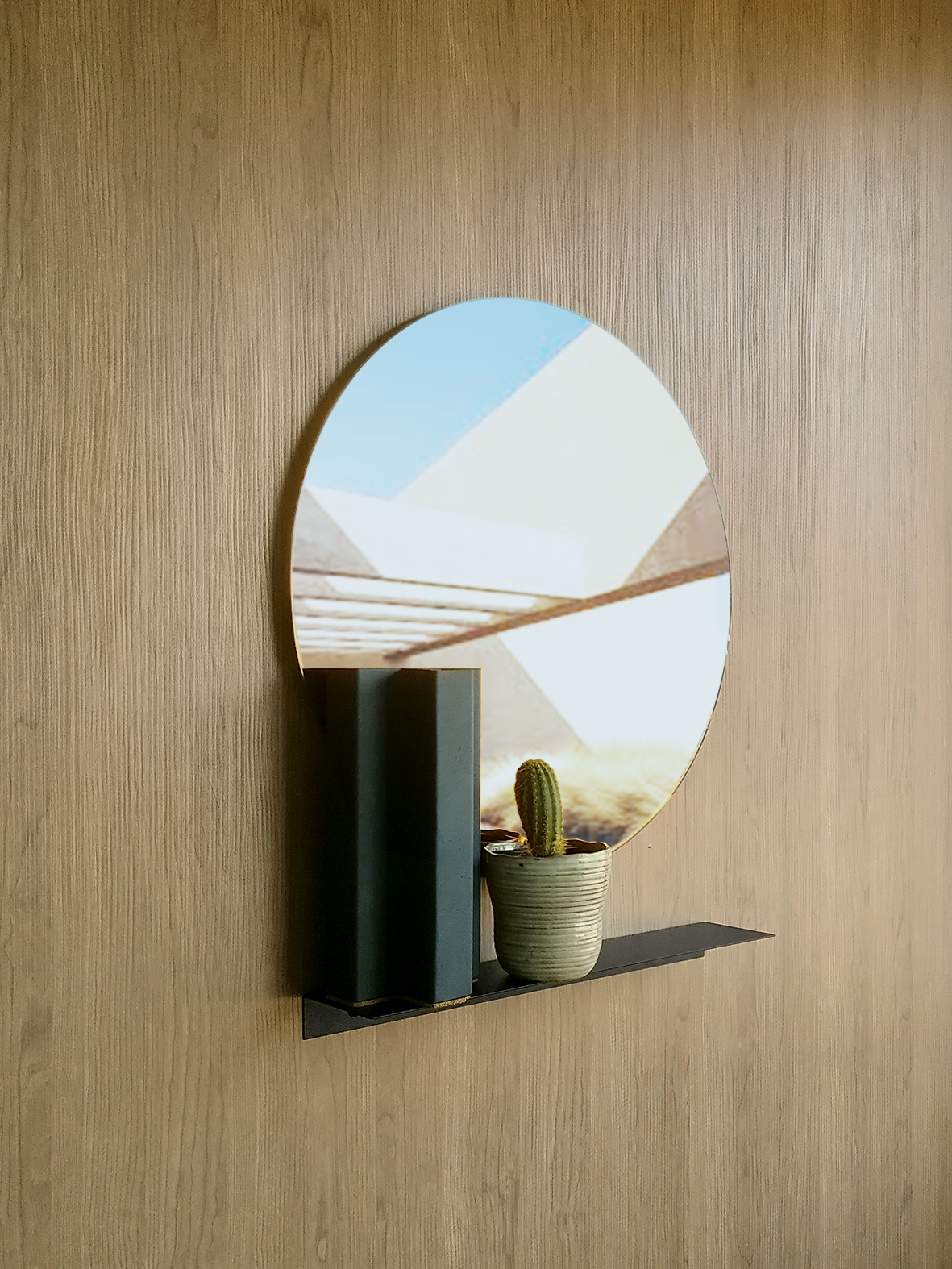 This round wall mirror is a large wall mirror in silver colour. It is a wall mirror above a black steel shelf. The steel shelf has a south african design vase and an indoor plant.