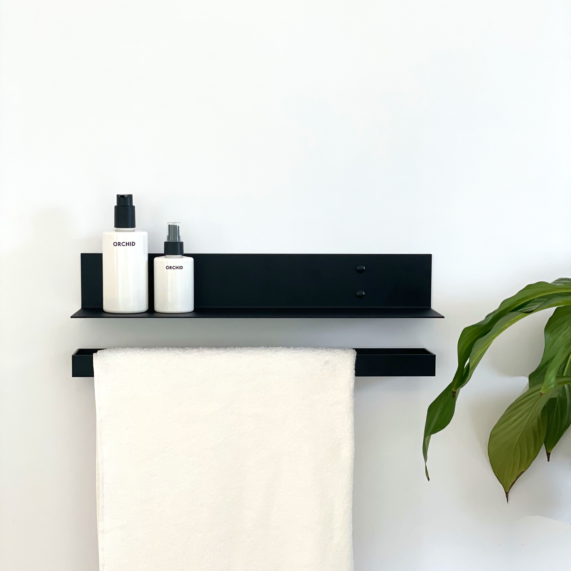 A black steel shelf with soap dispensers above a black towel rail with a white towel in a modern bathroom design