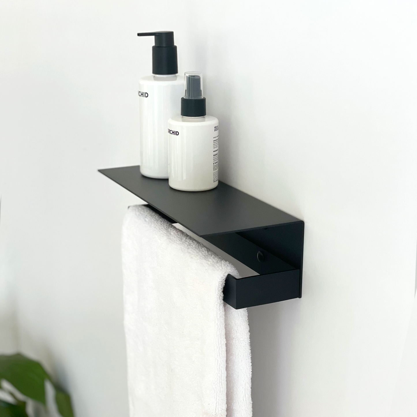 A black steel shelf with soap dispensers from Mr Price Home. The modern bathroom shelf sits above a black steel towel rail hanging a white towel in a modern bathroom design in Johannesburg