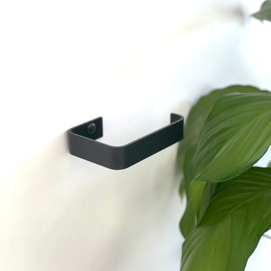 A black steel toilet paper holder or black metal toilet roll holder in a modern bathroom design store in Johannesburg with a indoor bathroom plant from Mr price home