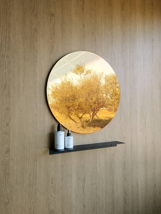 A big beautiful round wall mirror in a luxury bathroom design in Johannesburg. The large round mirror has a reflection of nature. The gold round mirror hangs above a black steel shelf. The shelf for bathroom holds two soap dispensers from Mr Price Home