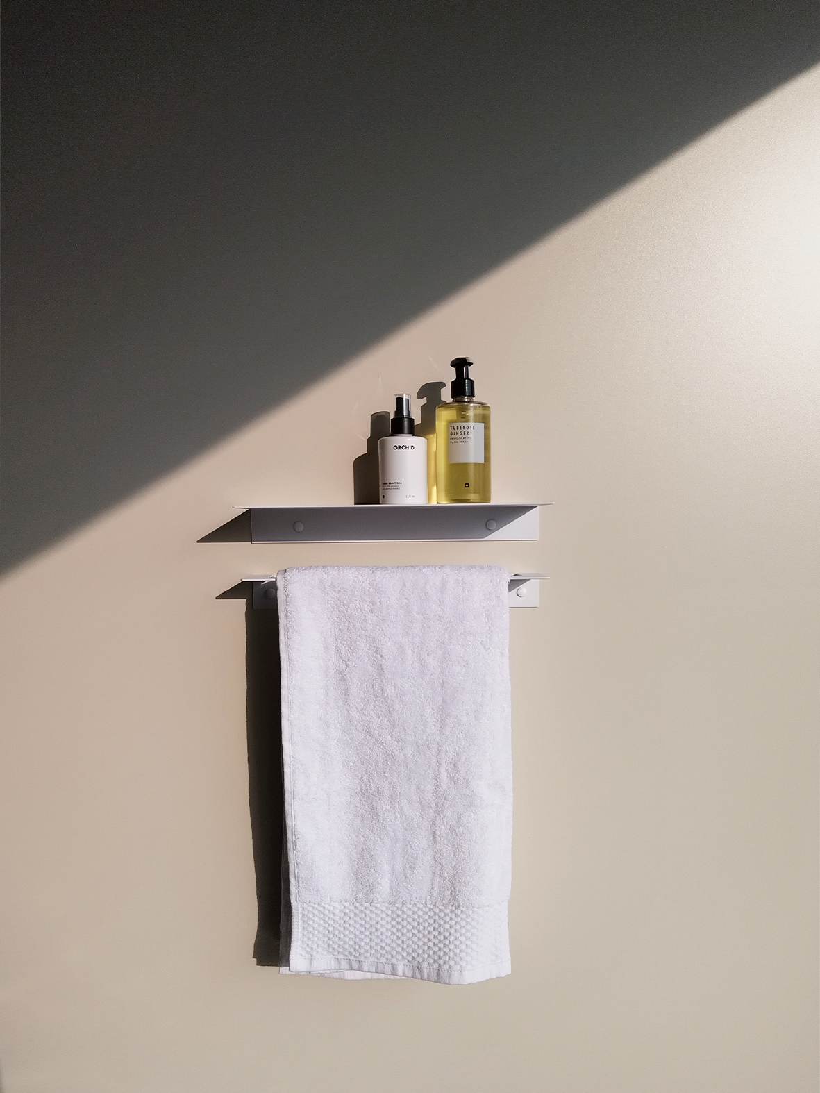 a white steel bathroom shelf with two soap dispensers from Mr Price home hanging above a white steel towel rail in a modern bathroom design store in Johannesburg