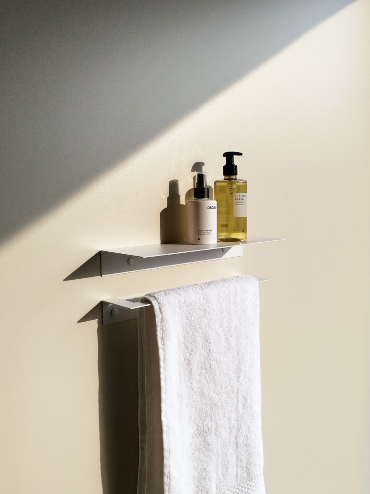 A white steel bathroom shelf with soap dispenser from Mr Price Home above a white steel towel rail hanging a white bathroom towel in a South African furniture design store in Johannesburg