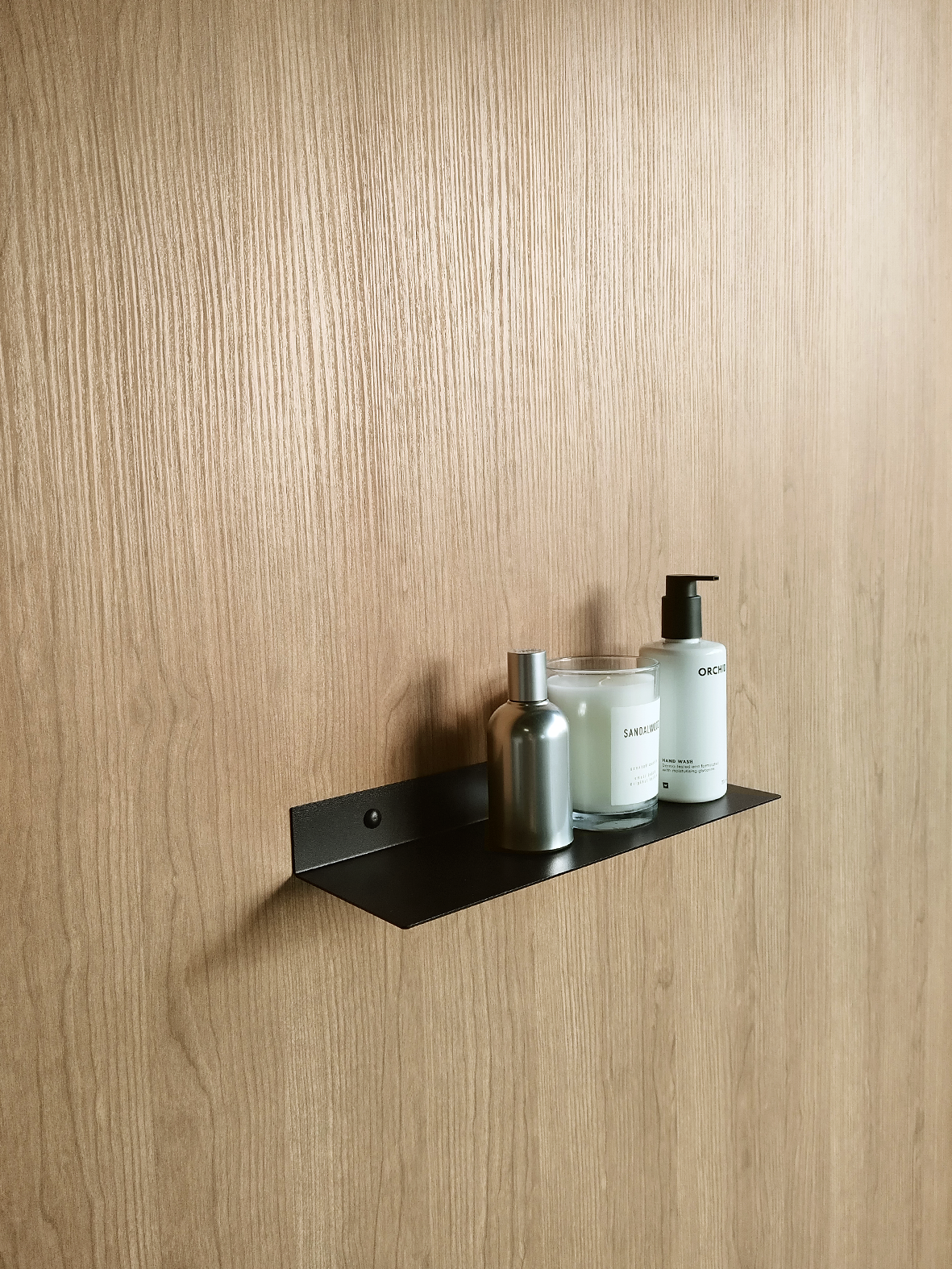 a black steel shelf or black metal bathroom shelf in a luxury bathroom design in johannesburg.  the black metal towel shelf holds a soap dispenser from Mr Price Home and a candle from Mr Price home. The bathroom shelf also holds a stainless steel soap bottle.