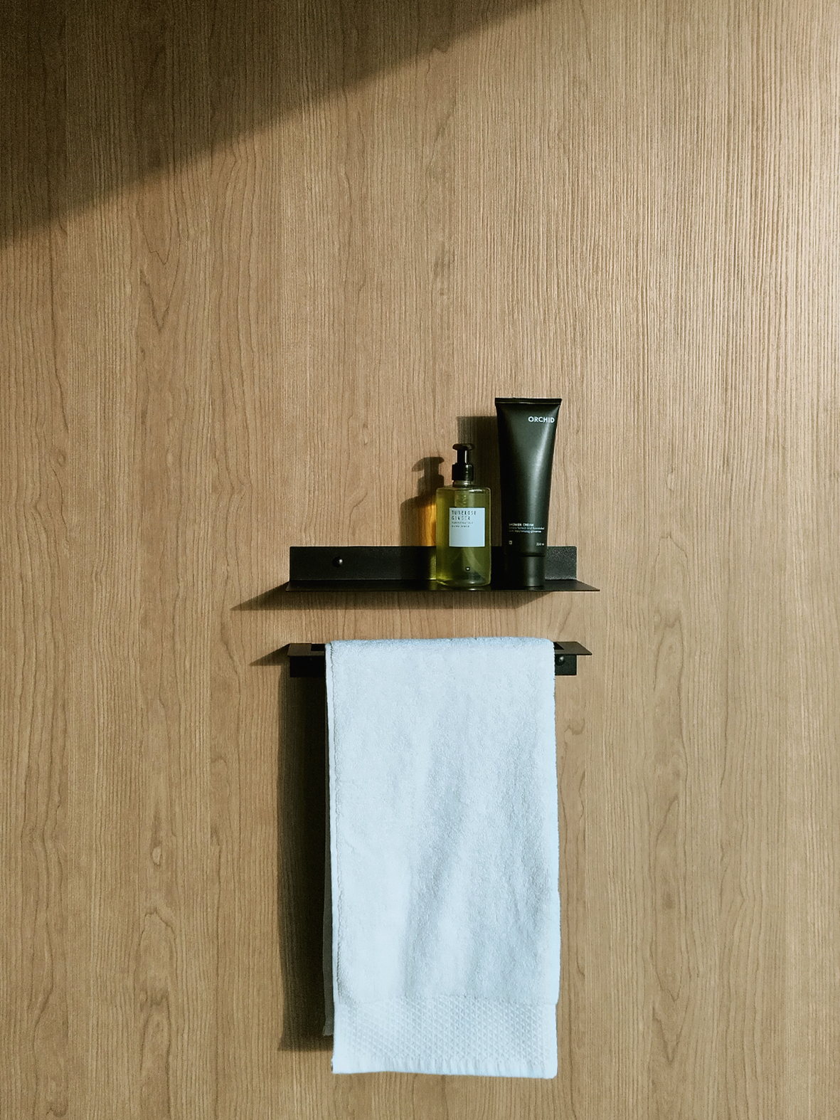 A black steel bathroom shelf with a soap dispenser and shampoo bottle from Mr Price Home above a black steel towel rail or towel ladder hanging a white towel in a luxury bathroom design store in Johannesburg